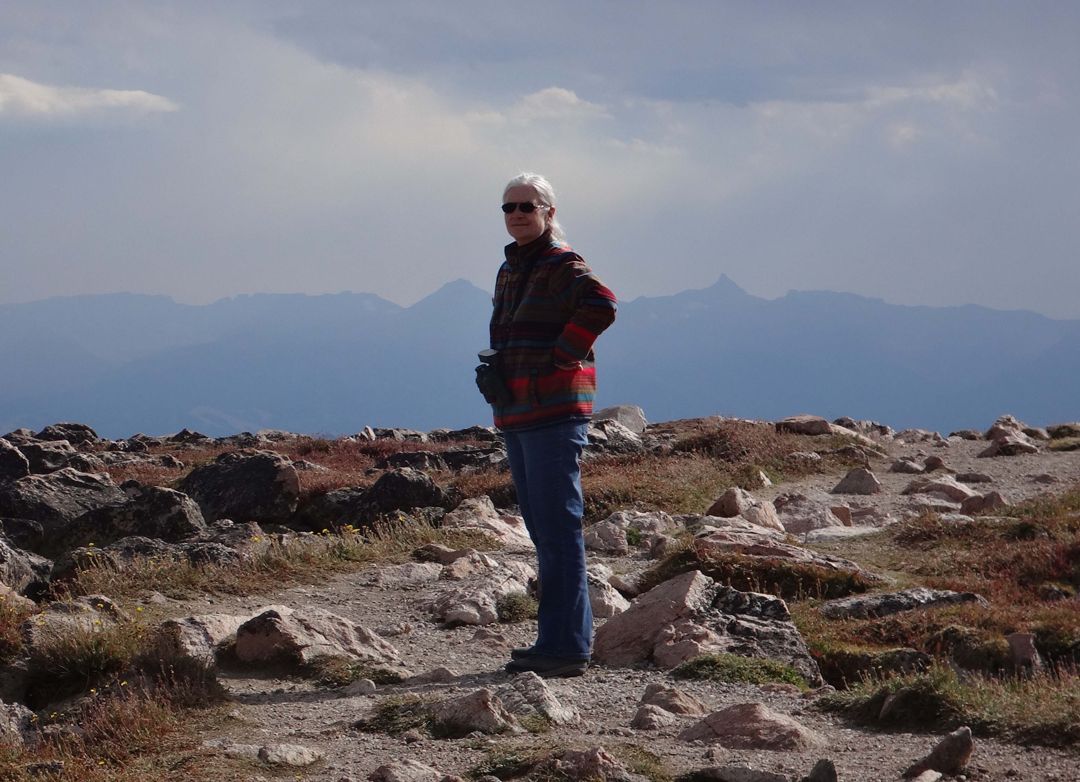 Dr. Horton stands among shrubs in front of mountains and turns back to look at the camera